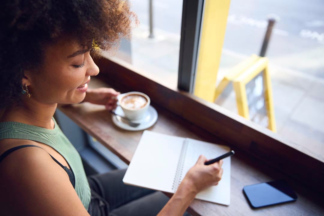 woman drinking coffee and writing in a notebook