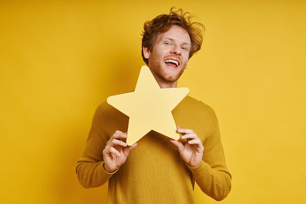 redhead man holding star shape banner and smiling against yellow background