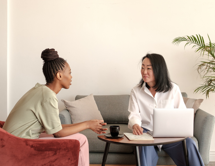Two woman sitting one is working and the other one is looking at her to represent client and agent relationship
