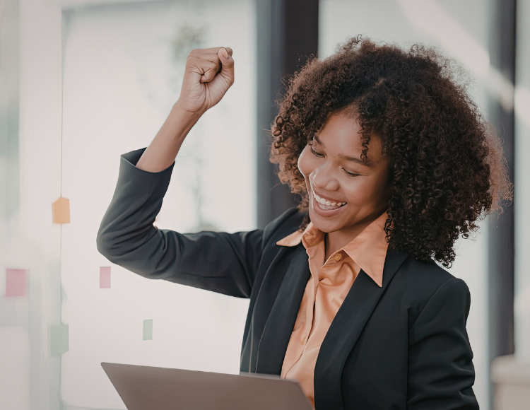 Woman celebrating a win watching her laptop and throwing her fist up in the air