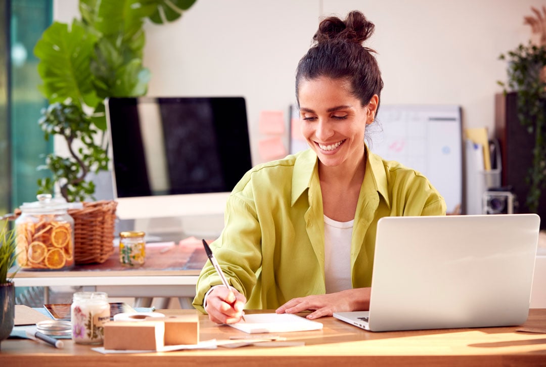 Woman RWriting Thank You Notes At Home Working On Laptop