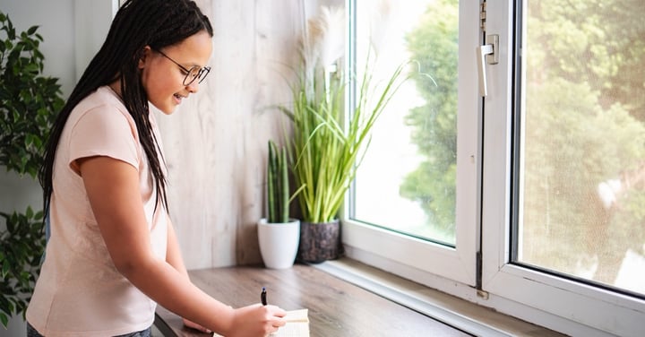 Teenage girl with braided hair writing in a journal by a window