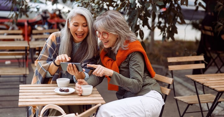 Two smiling women enjoying a mobile phone at cafe