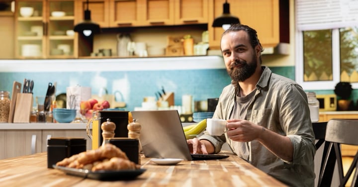 Bearded man working on laptop at home kitchen table