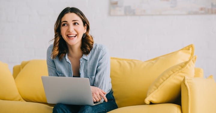 Smiling woman working on laptop from yellow couch