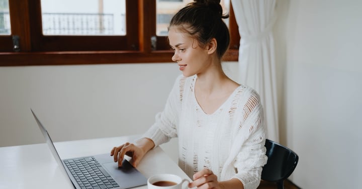 Woman works on laptop and drinks tea indoors