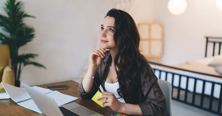 Thoughtful woman working at desk with laptop