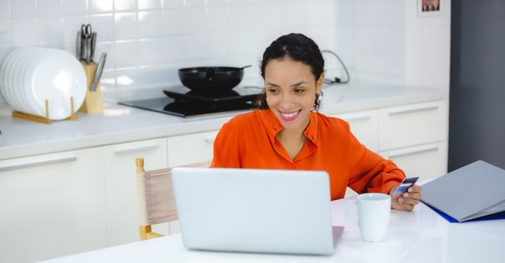 Woman uses laptop and credit card in kitchen