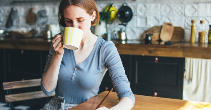 Woman writing in a notebook with a coffee cup