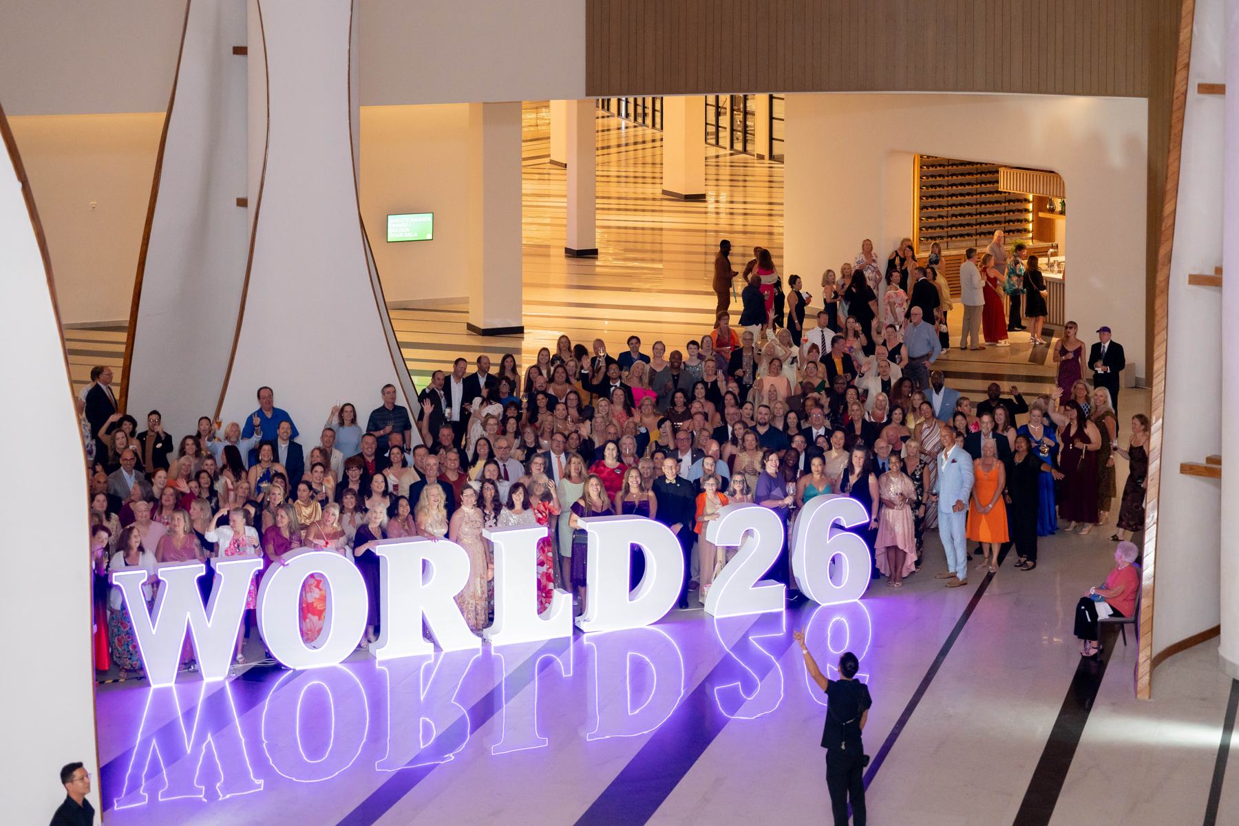 Members gathered around the illuminated WORLD26 letters